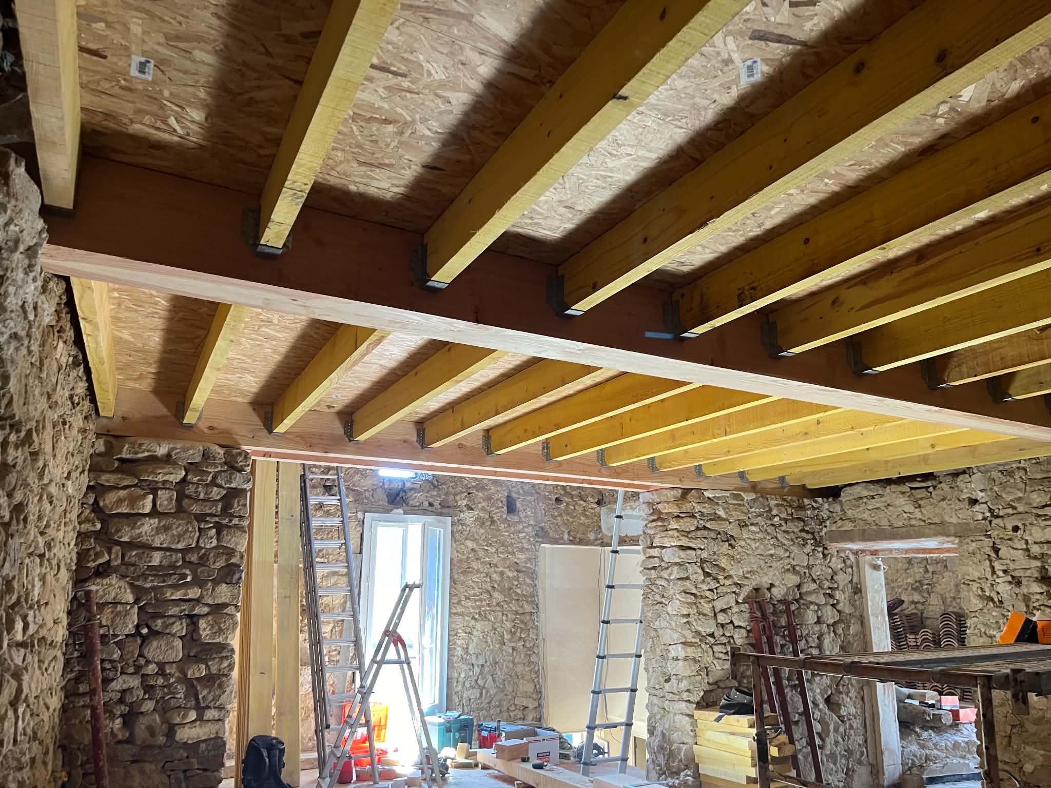 Solivage neuf installé dans un intérieur aux murs de pierre